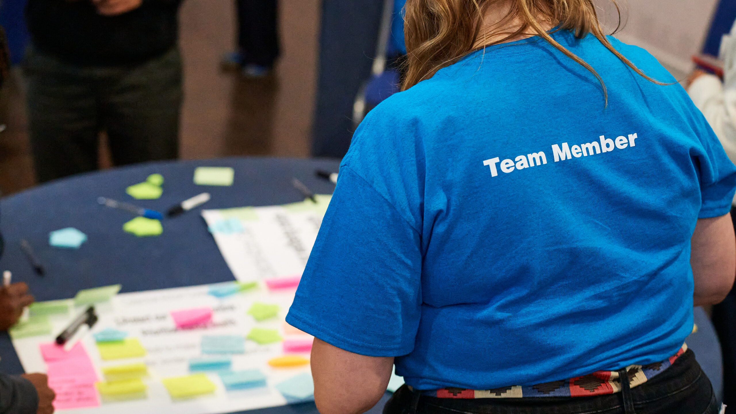 Photograph of the back of a person with brown hair from The Childhood Trust with a blue t-shirt with the words 'Team Member' printed in white
